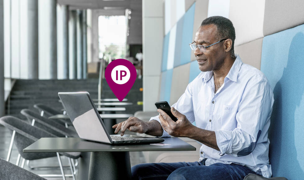 Meneer die aan het werk is achter een laptop met tegelijk mobiel in de hand